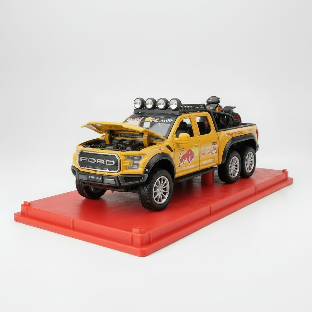 A yellow die-cast model pickup truck with an open hood, displayed on a red base. The model features Red Bull Racing graphics and is photographed in a home or office setting with a clear display case in the background.